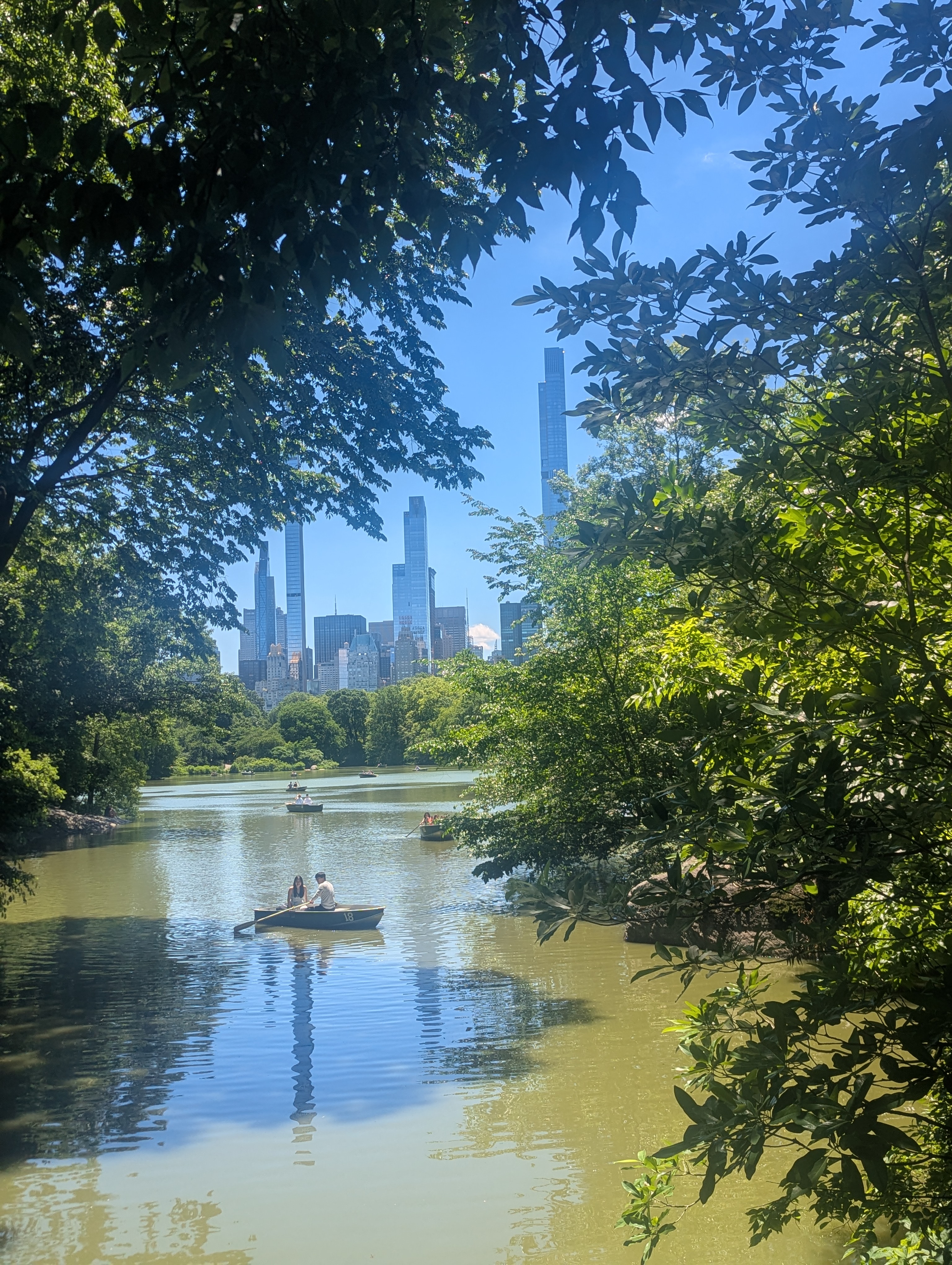 People rent boats to row through one of the lakes. You can see the Manhatten skyline.